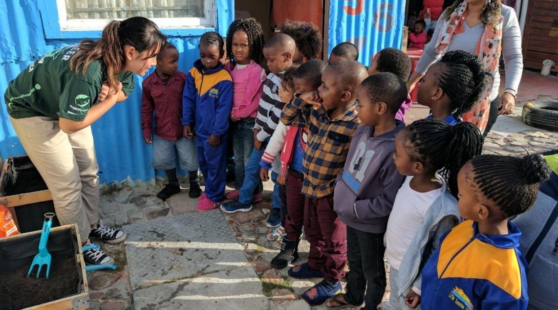 An intern from Projects Abroad is talking to a group of children promoting healthy eating and teaching them how to grow vegetables as part of her nutrition internship in South Africa. A female intern from Projects Abroad is pictured teaching a group of children about growing vegetables as part of her nutrition internship in South Africa.
